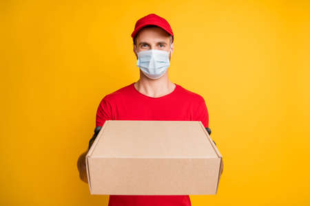 Photo of calm postman hold carton box give you wear mask red t-shirt headwear isolated yellow color...