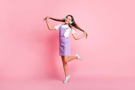 Full length photo of little kid girl with wireless headset hold straight hairdo isolated over pastel color backgroundの写真素材
