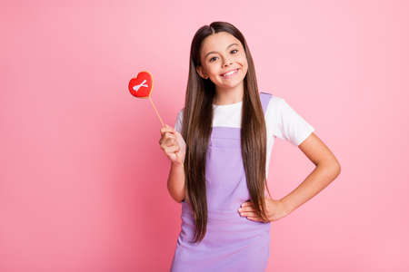 Portrait of pretty kid lady hols heart shape lollipop wear white violet overall isolated over pastel color backgroundの写真素材