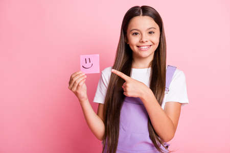 Photo of positive kid girl point finger happy emoticon sticker wear white violet overall isolated on pastel color backgroundの写真素材