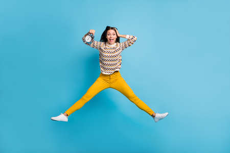 Full length photo of funny young lady wear ornament sweater jumping hand head holding clock isolated blue color backgroundの写真素材
