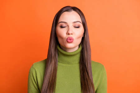 Portrait of optimistic brunette hairdo girl blow kiss closed eyes wear green sweater isolated on pumpkin color backgroundの写真素材