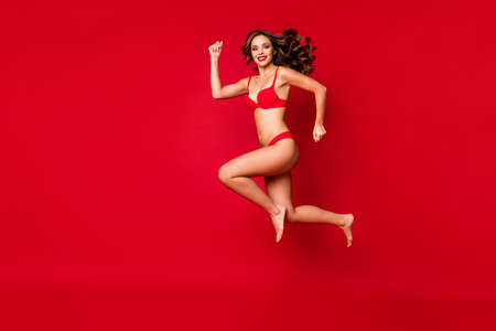Full length body size view of nice attractive lovable slim fit sporty thin bare foot purposeful cheerful wavy-haired girl jumping running isolated on bright vivid shine vibrant red color backgroundの写真素材