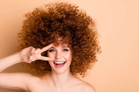 Close up photo beautiful she her no clothes nude lady curls fashion procedure stylist perms roller curlers salon hold hand arm near eye show v-sign say hi sincere isolated beige pastel backgroundの写真素材