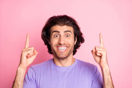 Photo of funny young guy direct fingers up empty space wear purple shirt isolated pastel pink color...