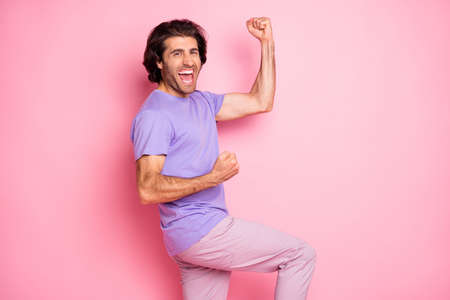 Photo of funny bristled guy raise fists knee open mouth wear violet shirt pants isolated pastel pink...