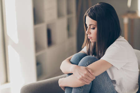 Profile side photo of attractive young girl feeling upset hug her knees sitting couch in house indoorsの写真素材