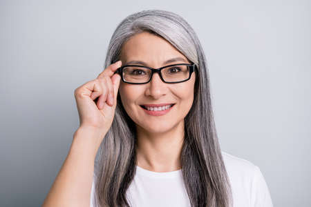 Photo of retired woman toothy smile look camera hold specs wear eyeglasses white t-shirt isolated grey color backgroundの写真素材