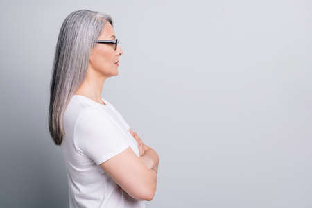 Profile photo of retired woman look empty space crossed arms wear spectacles white t-shirt isolated...