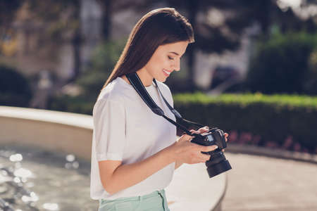 Photo portrait of woman holding digital photo camera with two hands checking results outdoors