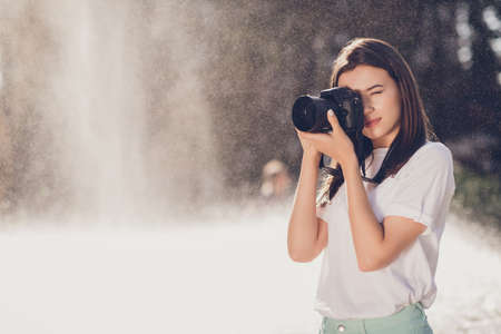 Photo portrait of serious woman taking a shot holding digital camera with two hands outdoors with...