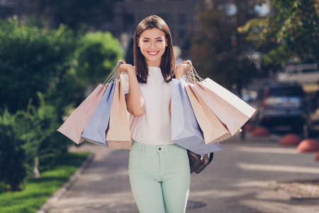Photo portrait of excited girl carrying many shopping bags outsideの写真素材