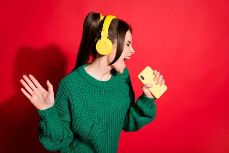 Photo of cute young lady wear green knitted pullover listening music headphones singing isolated red color backgroundの写真素材