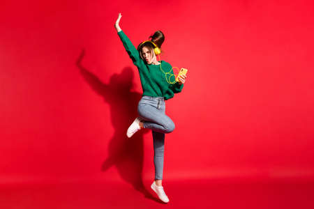 Full length photo of sweet young woman dressed green knitted sweater headset dancing jumping isolated red color backgroundの写真素材