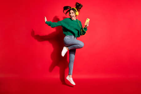 Full length photo of charming young woman dressed green knitted sweater headset dancing jumping isolated red color backgroundの写真素材
