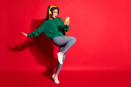 Full length photo of sweet young lady wear green knitted pullover listening music headphones dancing empty space isolated red color backgroundの写真素材