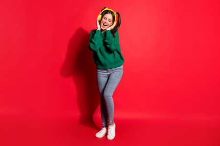 Full length photo of adorable sweet young woman dressed green knitted sweater arms headset singing isolated red color backgroundの写真素材