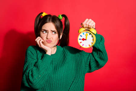 Portrait of young attractive unhappy upset annoyed female look at clock pout lips isolated on red color backgroundの写真素材