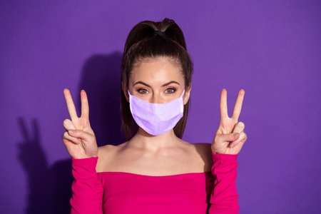 Photo of candid sweet girl two hands make v-sign wear medical respiratory isolated over violet color backgroundの写真素材