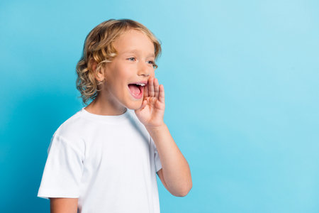 Photo of small boy screaming into empty space wear casual style clothes isolated over blue color backgroundの写真素材