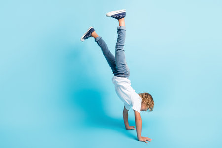Full length photo of little kid stand hands raise legs wear white shirt jeans sneakers isolated blue color backgroundの写真素材