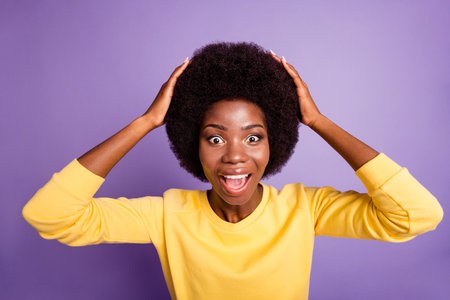 Portrait of astonished dark skin girl scream touch hands hairdo wear yellow pullover isolated on violet color backgroundの写真素材