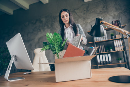 Low angle view photo of frustrated girl put keyboard in cardboard box cry dont want quit job company bankrupt corona virus crisis wear blazer jacket in workstation loftの写真素材