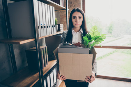 Photo of frustrated stressed depressed girl ceo expert lose job hold cardboard box with folders wear blazer jacket suit in workplace workstationの写真素材