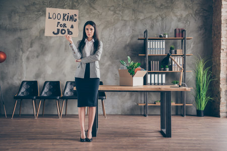 Full length photo of frustrated girl ceo marketer girl lose job search look for work in coronavirus quarantine crisis hold cardboard text wear blazer suit stilettos in workplace workstationの写真素材