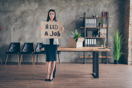 Full body photo of upset sad girl lose job company covid crisis bankrupt hold cardboard text wear blazer suit high-heels in workplace workstationの写真素材