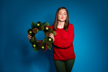 Portrait of her she nice attractive pretty dreamy lovable girl holding in hands fir cone festal traditional wreath sending air kiss isolated bright vivid shine vibrant blue color backgroundの写真素材