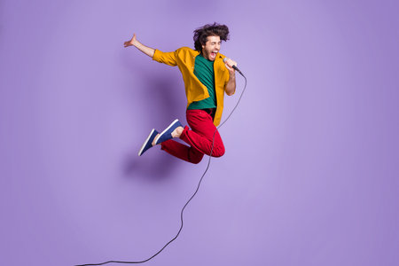 Full length photo portrait of crazy guy jumping up singing into microphone isolated on vivid violet colored backgroundの写真素材