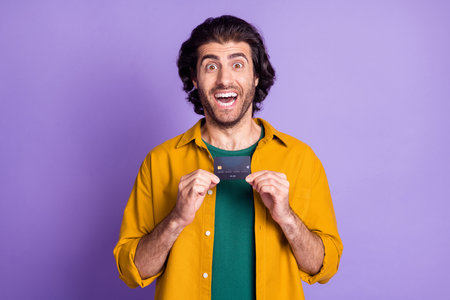 Photo portrait of man holding credit card in two hands with open mouth isolated on vivid purple colored backgroundの写真素材