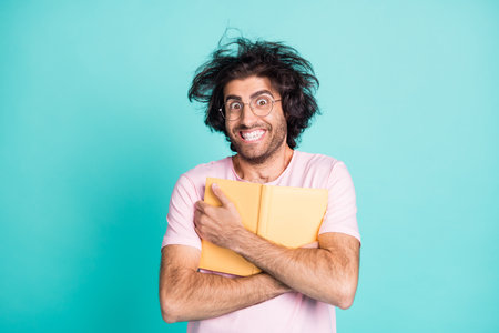 Photo of weird hairstyle satisfied man arms hold cuddle book to chest toothy smile isolated on turquoise color backgroundの写真素材