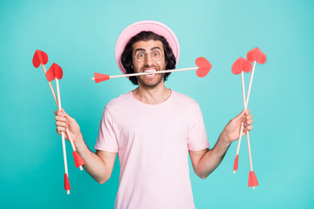 Photo of surprised hipster man hold arrows wear pink cap spectacles t-shirt isolated on teal color backgroundの写真素材