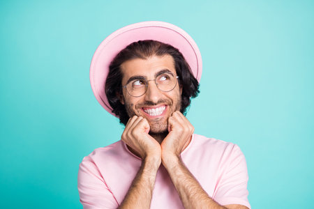 Portrait of good-looking optimistic guy looking empty space wear spectacles cap pink outfit isolated on teal backgroundの写真素材