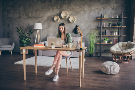 Full size photo of optimistic girl type laptop from home wear green shirt trousers sneakers indoorsの写真素材