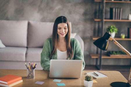 Photo of optimistic nice girl work on laptop from home wear green shirt indoorsの写真素材