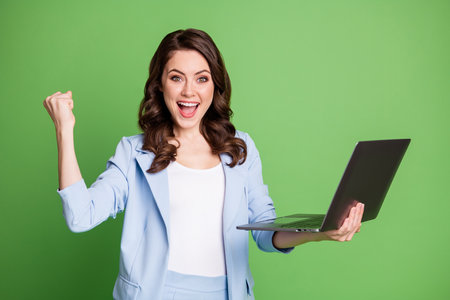 Portrait of smart female worker holding laptop smiling cheerfully wearing blue formal suit isolated on bright green color backgroundの写真素材