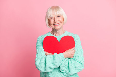 Photo portrait of cute grandmother hugging embracing red heart symbol valentines day isolated on pastel pink color backgroundの写真素材