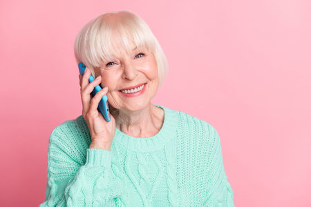 Photo portrait of happy grandmother smiling talking on mobile phone communicating isolated on pastel pink color backgroundの写真素材