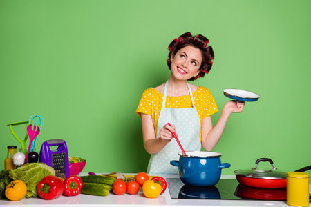 Portrait of her she nice attractive mature glamorous cheerful dreamy housewife cooking domestic meal dish lunch cuisine stirring soup fantasizing isolated over green pastel color backgroundの写真素材