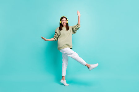 Full length photo portrait of cheerful dancing girl wearing headphones standing on one leg isolated on vivid teal colored backgroundの写真素材