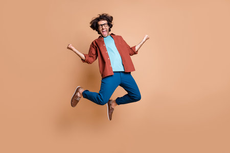 Full length photo portrait of wild guy celebrating jumping up isolated on pastel beige colored...