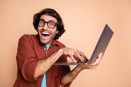 Photo portrait of mad hacker typing holding laptop in hand isolated on pastel beige colored...