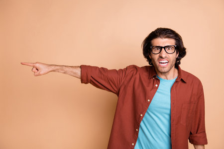 Photo of aggressive man indicate finger away wear spectacles brown t-shirt isolated beige color backgroundの写真素材