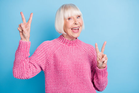 Photo portrait of excited cheerful old lady showing two v-signs isolated on pastel blue colored backgroundの写真素材