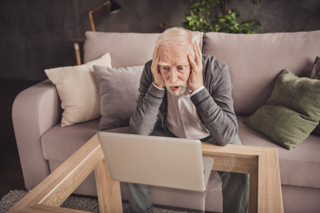 Photo of depressed pensioner wear grey cardigan sitting arms head watching modern gadget indoors...