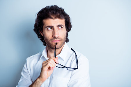 Photo portrait of minded guy looking at blank space touching face chin with glasses taken off...