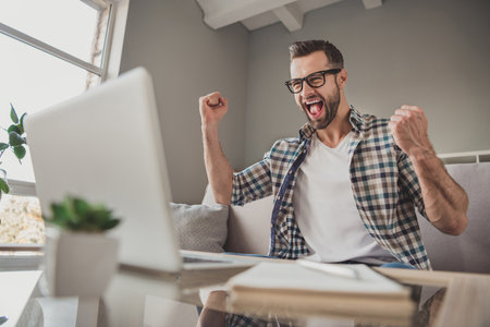 Photo of young excited man happy positive smile celebrate win victory success fists hands sit sofa home remote workの写真素材